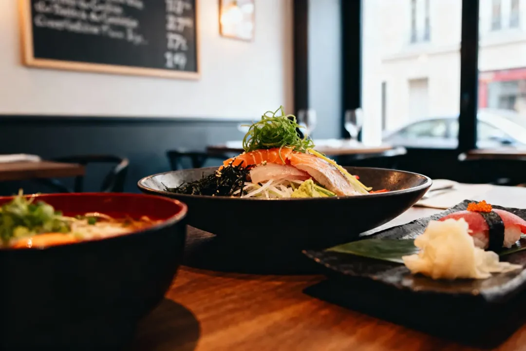 Assiette de sushi et sashimi dans un restaurant, présentation élégante sur table en bois. Ambiente moderne et lumineux.