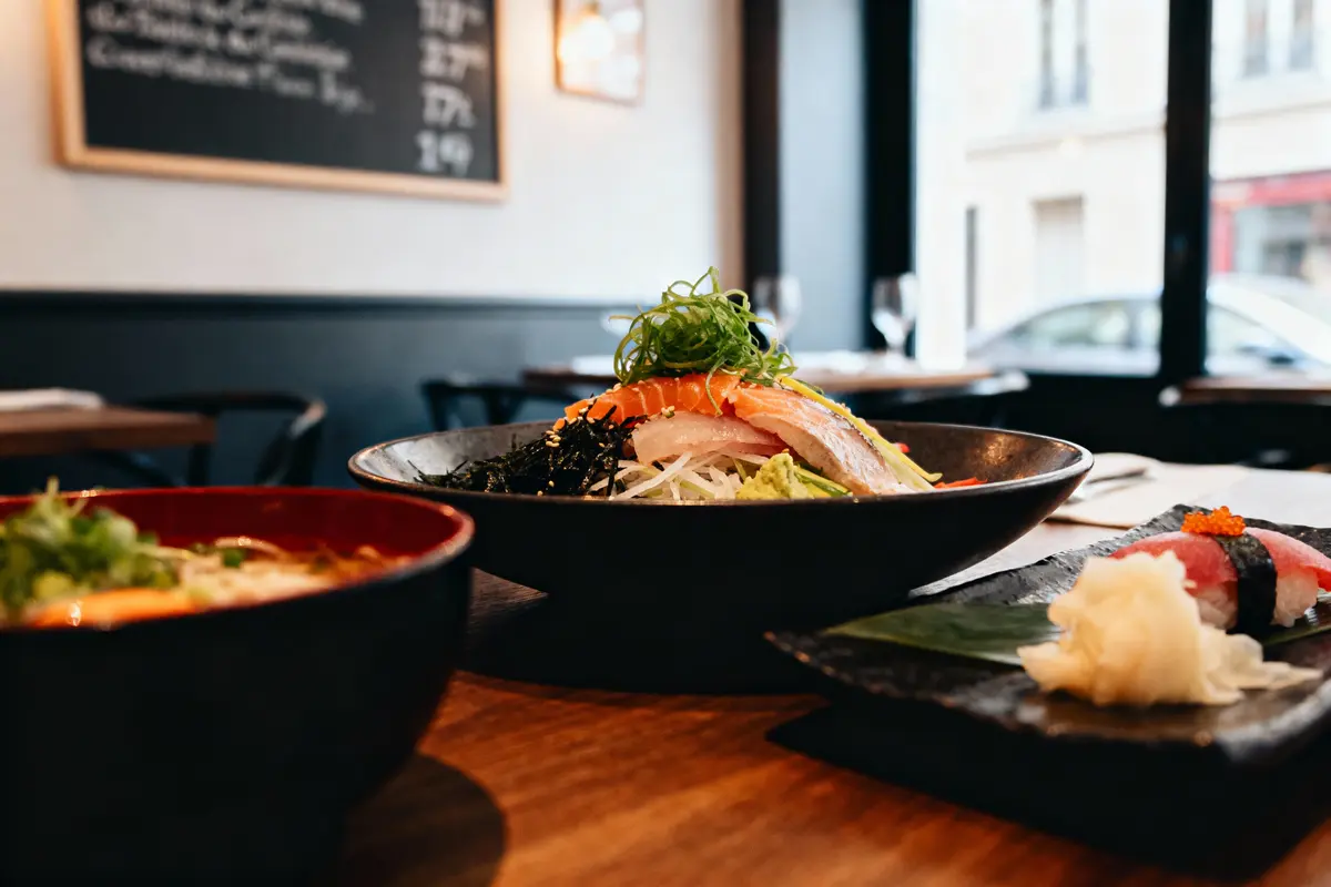 Assiette de sushi et sashimi dans un restaurant, présentation élégante sur table en bois. Ambiente moderne et lumineux.