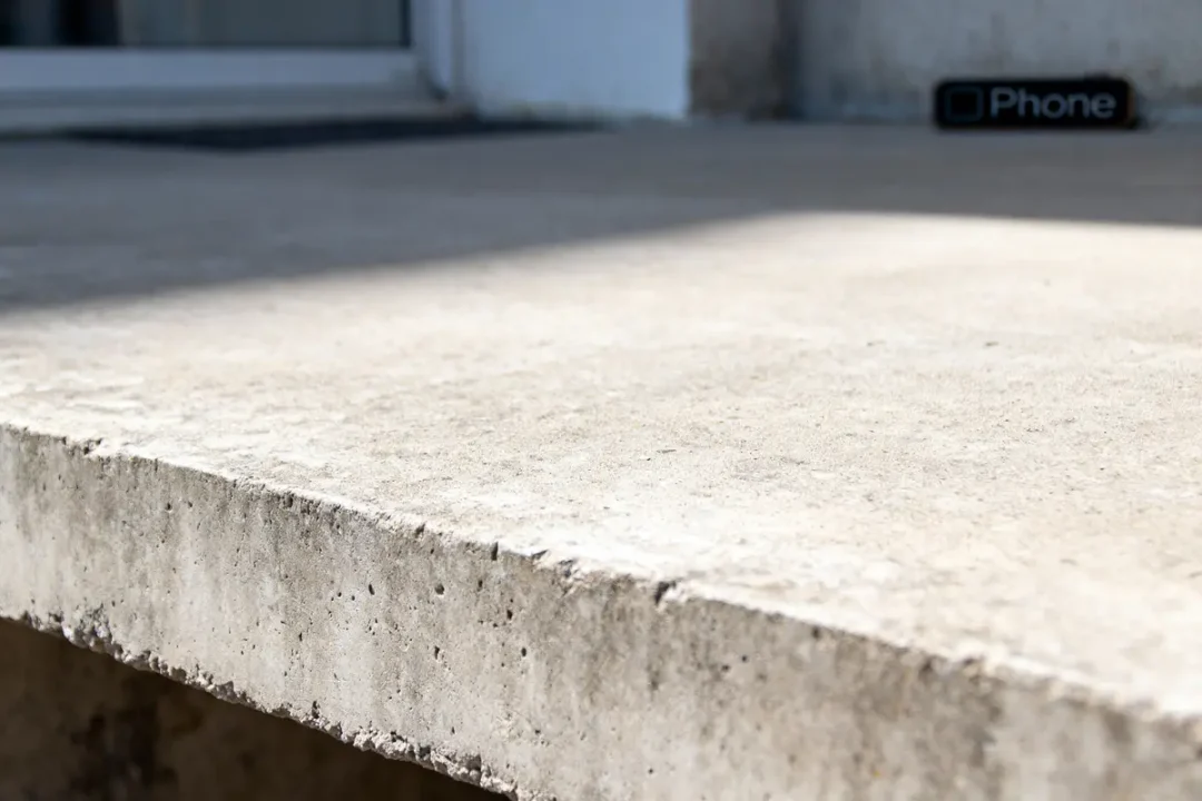 Bordure en béton en gros plan avec des ombres, objet noir avec mot "Phone" en arrière-plan.