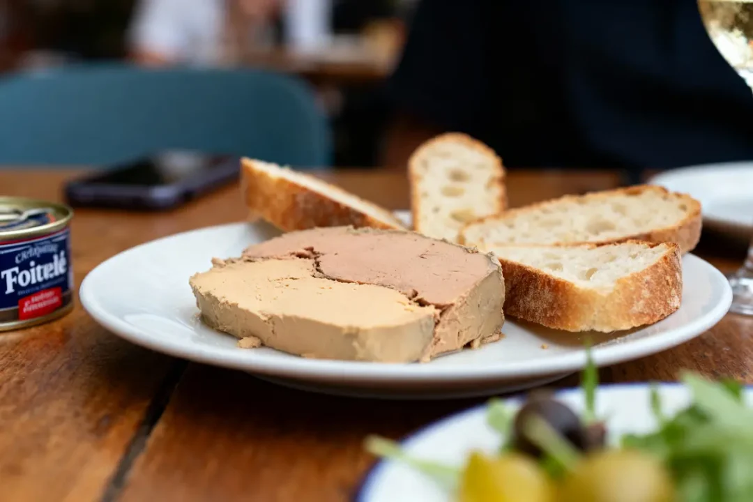 Assiette avec foie gras et tranches de pain, boîte de conserve et verre de vin en arrière-plan.