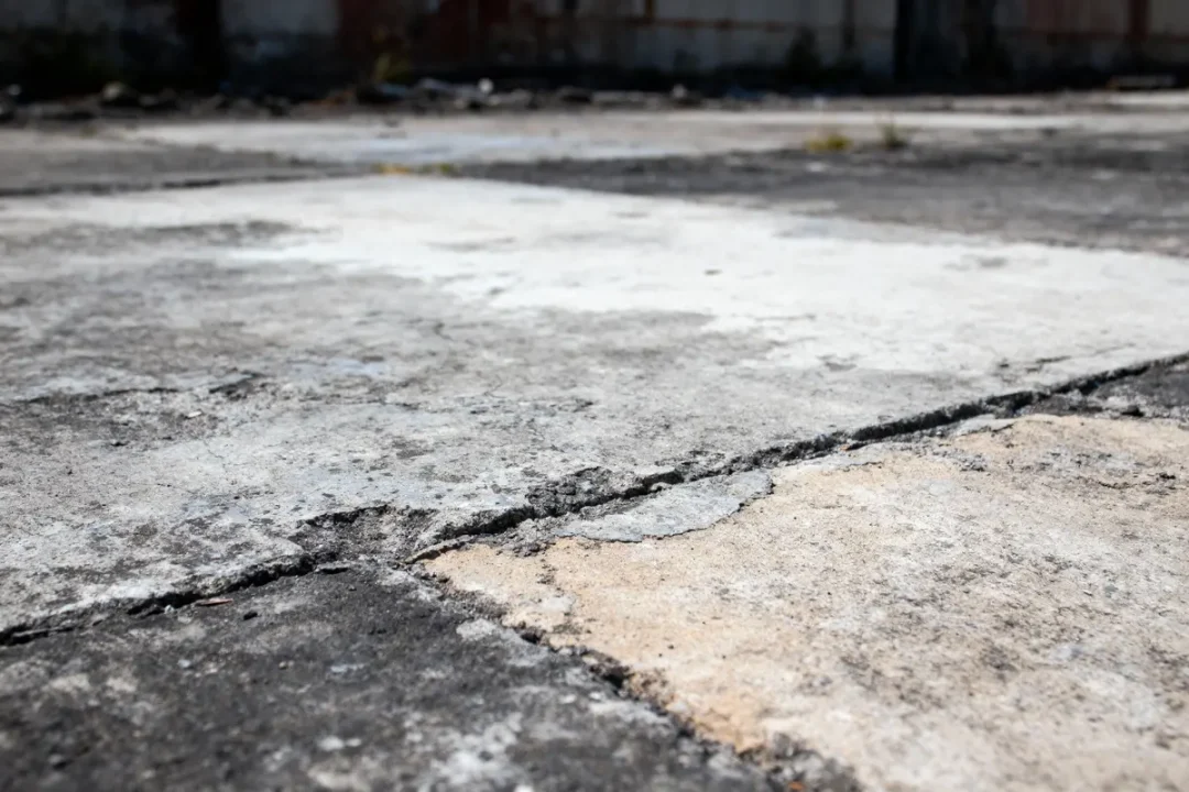Gros plan d'un sol en béton fissuré, surface usée et dégradée, légèrement ensoleillée.