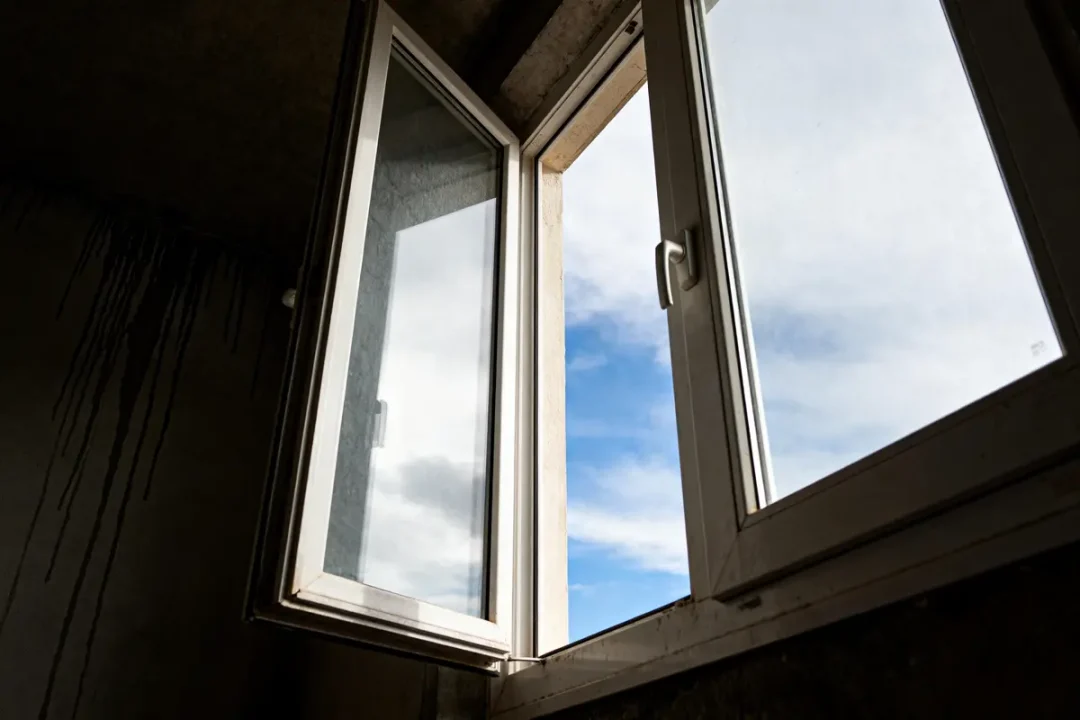 Fenêtre ouverte vers un ciel bleu nuageux, mur intérieur sombre en second plan.
