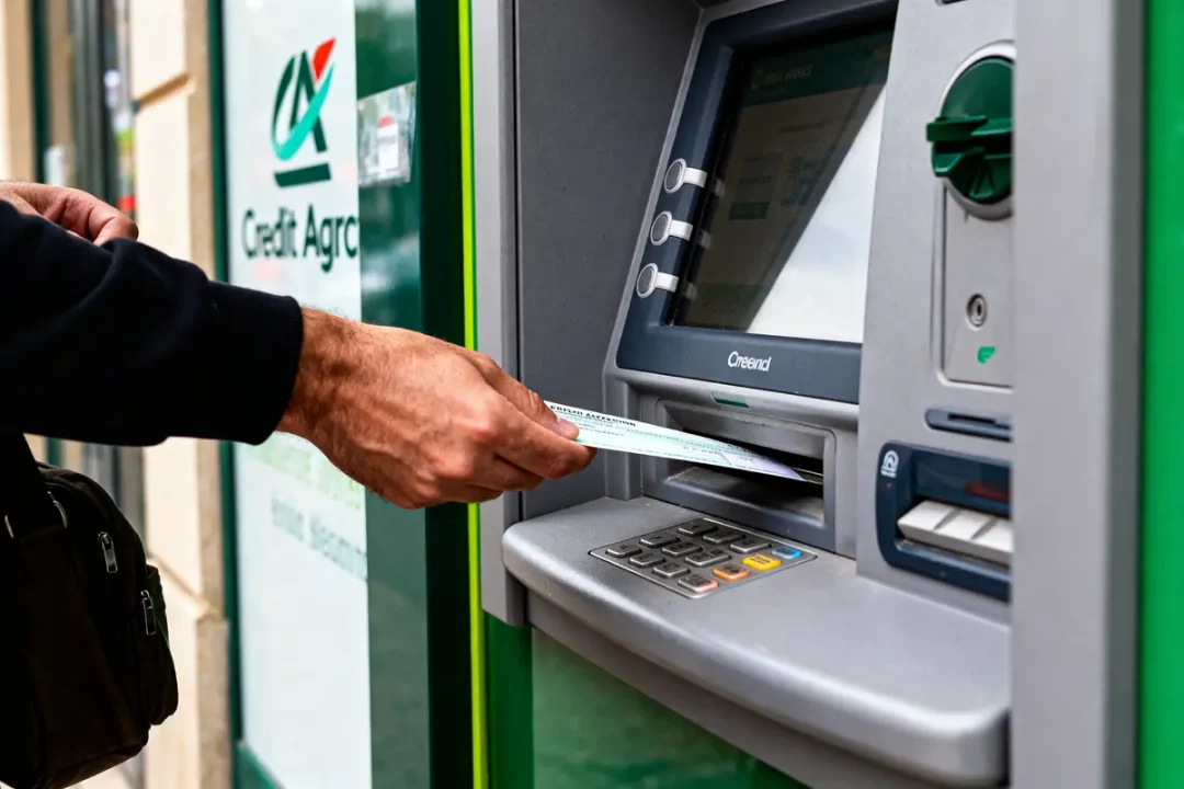 Une main insère un document dans un distributeur automatique Crédit Agricole.