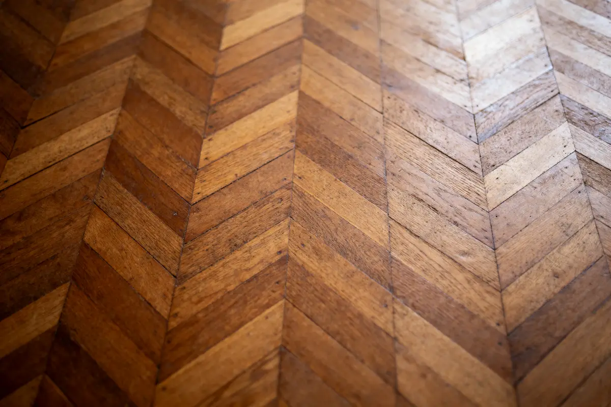 Plancher en bois avec motif en chevrons, teintes marron clair et foncé, perspective vers l'avant.