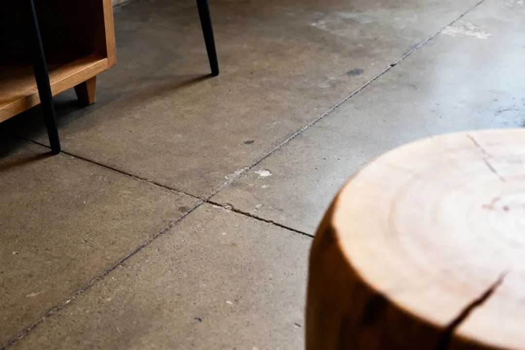 Sol en béton, coin de meuble en bois et tronc d'arbre en intérieur minimaliste.