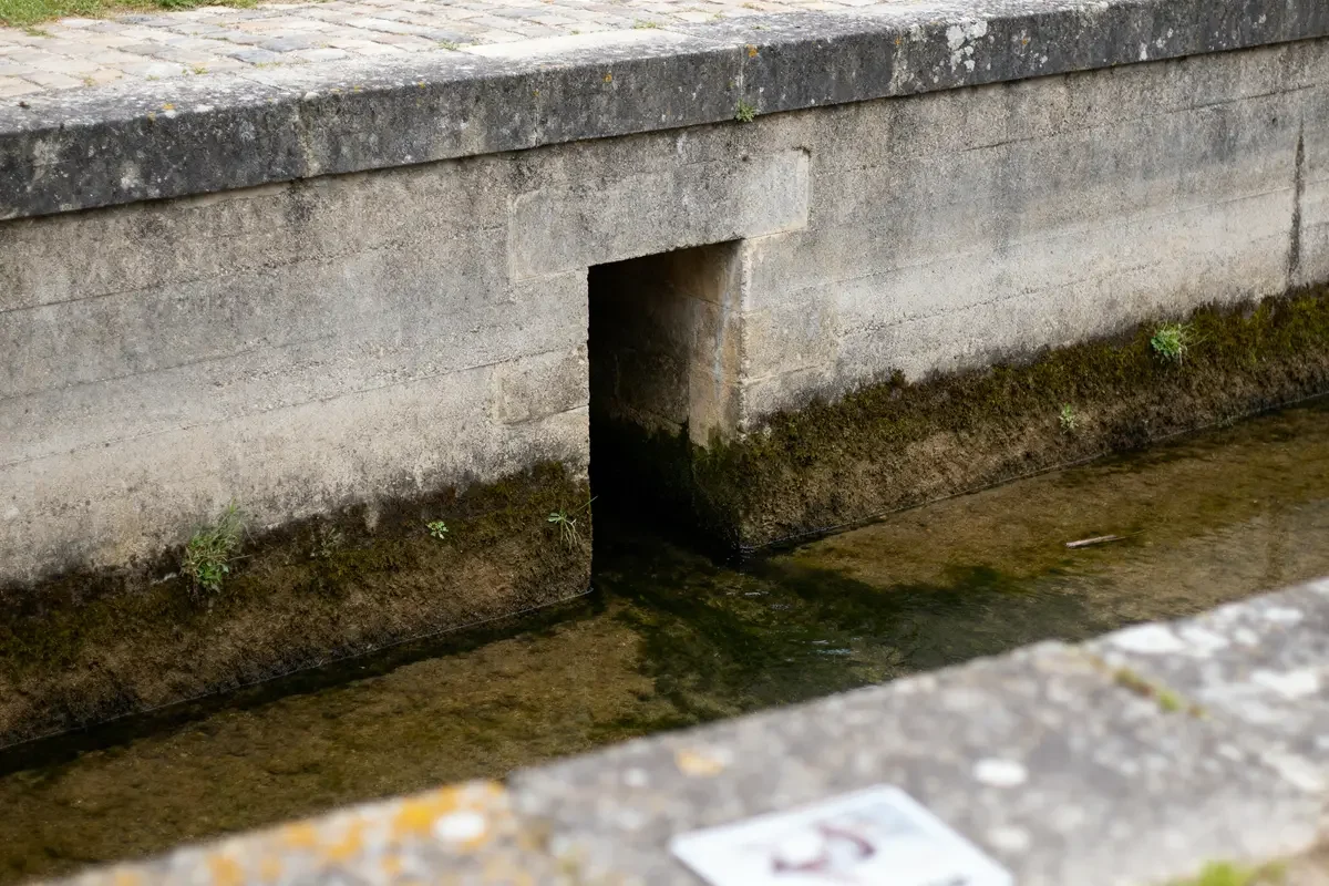 Ouverture d'une barbacane en pierre au-dessus d'un cours d'eau.