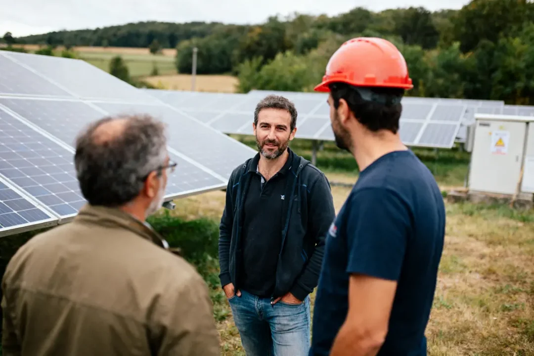 Trois hommes discutant devant des panneaux solaires dans un champ verdoyant, ambiance professionnelle et sereine.